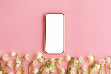 Beyaz ekranlı akıllı telefon ve pembe kağıt üzerinde bahar çiçekleri. Beyaz kar tanelerinin çiçekli yumuşak kenarı ve mesaj için yeri olan telefon şablonu. Mutlu kadınlar günü ya da anneler günü