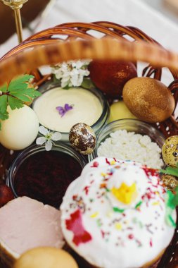 Şık paskalya yumurtaları, ev yapımı Paskalya ekmeği hasır sepetteki geleneksel Paskalya yemeği ve kırsal masada keten peçetede çiçek açan bahar çiçekleri. Mutlu Paskalyalar! Şenlikli kahvaltı.