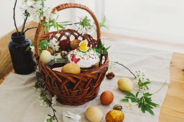 Şık paskalya yumurtaları, ev yapımı Paskalya ekmeği hasır sepetteki geleneksel Paskalya yemeği ve kırsal masada keten peçetede çiçek açan bahar çiçekleri. Mutlu Paskalyalar! Şenlikli kahvaltı.