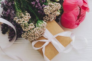 Anneler Günü ve Sevgililer Günü konsepti kutlu olsun. Beyaz ahşap arka planda şakayık, leylak ve gül desenli şık el sanatları hediye kutusu ve buket. Üst görünüm