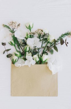 Zarftaki bahar çiçekleri düzdü. Süslü güller, ortanca ve okaliptüs dalları ve beyaz ahşap üzerinde el işi zarfından açan yapraklar. Merhaba bahar. Anneler Günü ve kadınlar günü konsepti kutlu olsun.