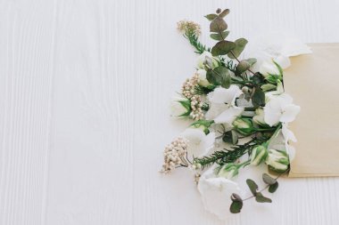 Süslü güller, ortanca ve okaliptüs dalları beyaz ahşap üzerinde çoğalarak çoğalıyorlar. Yaratıcı bahar görüntüsü, çiçekli tebrik kartı ve çiçek teslimatı