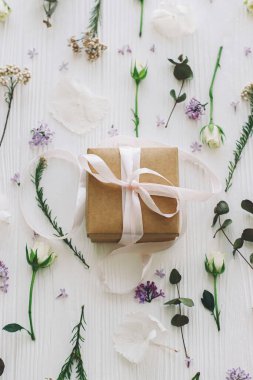 Leylak, gül, çiçek ve okaliptüs yapraklı şık bir hediye kutusu beyaz ahşap üzerine serilmiş. Anneler günün ve kadınlar günü konseptin kutlu olsun. Kurdele ve modern çiçek kompozisyonu olan bir el işi.