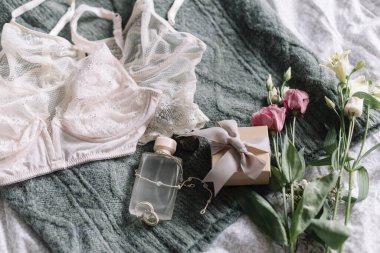 Şık bir hediye kutusu, modern mücevherler, parfüm şişesi ve yatağında bahar çiçekleri olan yeşil kazaklı dantel iç çamaşırı. Yumuşak ve modaya uygun kadınsı imaj. Mutlu Kadınlar Günü, kadın zorunlulukları