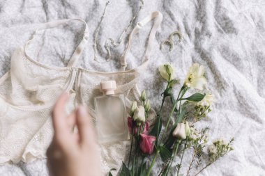 Şık bir parfüm şişesi, bulanık kadın eli dantel iç çamaşırı, modern mücevherler ve yatakta bahar çiçekleri. Koku konsepti, kadın esansları, parfüm. Yumuşak moda görüntü, şehvetli ruh hali