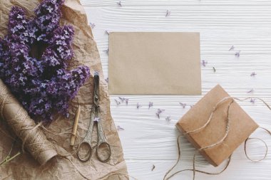 Şık bir kart, güzel leylak çiçekleri, hediye, antika makas, beyaz ahşap üzerinde kalem ve sicim, üst manzara. Hareketsiz bir hayat. Tebrik kartı şablonu, metin için boşluk. Anneler günün kutlu olsun..