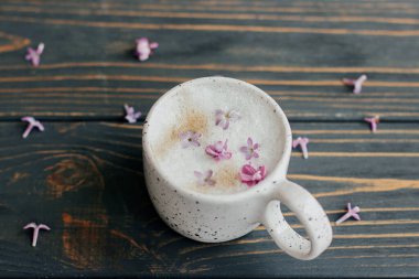 Koyu ahşap arka planda eflatun yapraklı kahve ve metin için yer var. Şık fincanda taze aromatik kahve ve kır ağacında bahar çiçekleri. Sabah ritüelleri