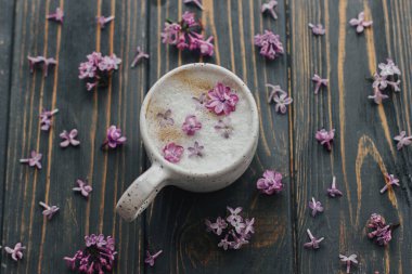 Koyu ahşap arka planda eflatun yapraklı kahve, yazı için yer, üst manzara. Şık fincanda taze aromatik kahve ve kırsal ahşap üzerinde mor taç yaprakları. Sabah ayinleri estetik