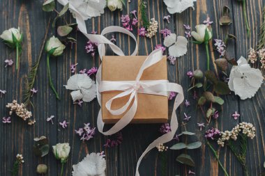 Basit bir hediye kutusu, kurdele ve leylak, okaliptüs, ortanca, koyu ahşap arka planda gül yaprakları. Bahar çiçekleri sergileniyor ve kır odunlarında sunuluyor. Anneler Günün kutlu olsun.