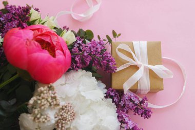 Modern taze buket ve parlak pembe arka planda kurdeleli basit bir hediye kutusu. Mutlu anneler günü ya da kadınlar günü, şık renkli tebrik kartı. Şakayık, leylak, okaliptüs, ortanca çiçeği.