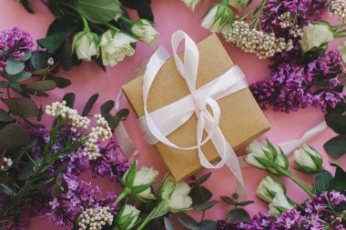 Basit bir hediye kutusu, kurdeleli ve güzel leylak ve gül çerçeveli parlak pembe arka planda yatıyordu. Mutlu anneler günü veya kadınlar günü, şık renkli tebrik kartı.