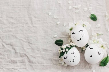 Şirin çiçek desenli komik yüzlü doğal yumurtalar çiçek açan bahar yaprakları ve yeşil yapraklarla keten kumaşın en üst görüntüsünü oluşturur. Mutlu Paskalyalar! Çevre dostu tatil konsepti. Metin için boşluk
