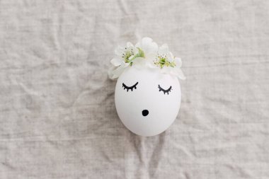 Doğal yumurta, uyuyan yüzü çizilmiş ve keten kumaşında çiçekli bir taç takıyor. Mutlu Paskalyalar! Çevre dostu sıfır atık tatil konsepti. Metin için boşluk olan üst görünüm