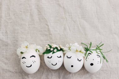 Mutlu Paskalyalar! Şirin çiçek desenli komik yüzlü doğal yumurtalar çiçek açan bahar yaprakları ve yeşil yapraklarla keten kumaşın en üst görüntüsünü oluşturur. Çevre dostu sıfır atık tatil konsepti. Metin için boşluk
