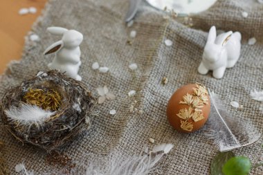 Kuru çiçek yapraklarıyla süslenmiş Paskalya yumurtası, tavşan ve yuvayı keten peçete, tüy ve kiraz çiçeğiyle sade bir masaya kurmuş. Paskalya yumurtalarının yaratıcı doğal çevre dostu dekoru. Mutlu Paskalyalar