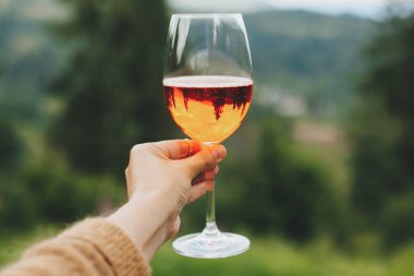 Dağların, ağaçların, yaz tatilinin ve tatil beldesinin arka planında lezzetli bir portakal kokteyli. Kadın aperol içkisiyle tezahürat yapıyor, dışarıda kutlama yapıyor.