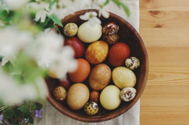 Tavşan heykelcikleri ve çiçek açan bahar çiçekleriyle ahşap kasede süslü paskalya yumurtaları. Metin için boşluk olan üst görünüm. Mutlu Paskalyalar! Sarı ve kırmızı renkte doğal boyanmış yumurtalar..