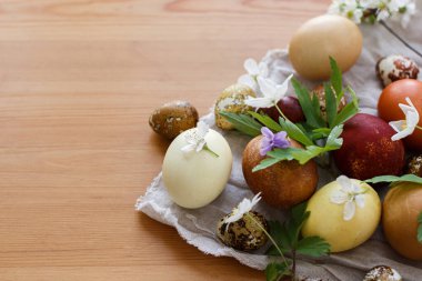 Modern pastel paskalya yumurtaları, bahar çiçekleri ve ahşap masa üzerindeki çarşaf örtüsü. Mutlu Paskalyalar! Çiçek açan şakayıklı gri tekstil üzerine doğal boyanmış yumurta. Metin için boşluk