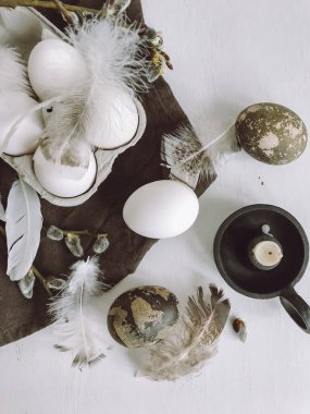 Easter rustic flat lay. Natural easter eggs, feathers, pussy willow branches, candle on cloth on white aged table.  Stylish rural still life. Modern simple aesthetics, white and grey colors