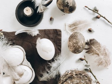 Easter rustic flat lay. Natural easter eggs, feathers, pussy willow branches, candle on cloth on white aged table.  Stylish rural still life. Modern simple aesthetics, white and grey colors