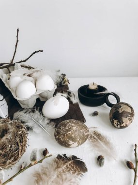 Simple stylish Easter still life. Natural easter eggs, soft feathers, pussy willow branches, bird nest on white rustic table. Modern Natural easter aesthetics, pastel beige and grey colors