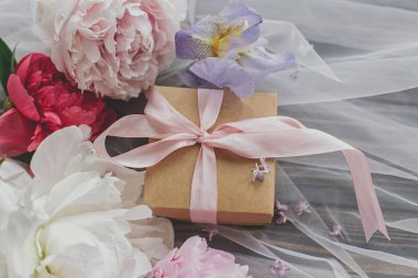 Anneler Günün kutlu olsun. Güzel şakayık, iren buketi ve yumuşak tül kumaşlı hediye kutusu. Ahşap kaplama, üst manzara. Hoş bir tebrik kartı. Pembe ve beyaz şakayıklar, mavi iris çiçeği ve hediye.