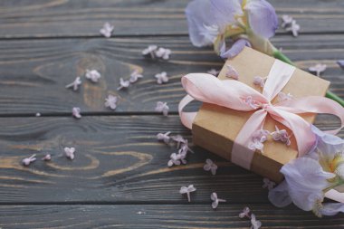 Güzel bir hediye kutusu, zambak çiçeği ve koyu ahşap arka planda leylak yaprakları, kopyalama alanı. Anneler Günün kutlu olsun. Mavi göz ve mor çiçekler ve hediye..