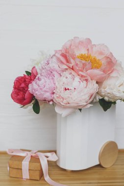 Modern şık vazoda güzel bir şakayık buketi ve ahşap arka planda hediye kutusu, kopyalama alanı. Anneler Günün kutlu olsun. Pembe ve beyaz şakayıklar ve hediye