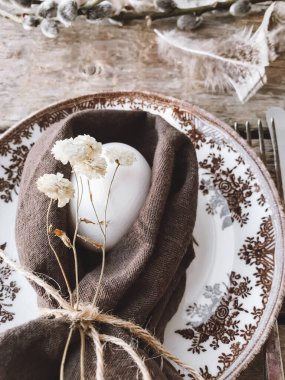 Şık bir paskalya sofrası. Peçeteli doğal paskalya yumurtası, klasik tabak ve çatal bıçak, yıllanmış ahşap masa üzerindeki yumuşak tüyler. Kırsal Paskalya natürmortu. Mutlu Paskalyalar