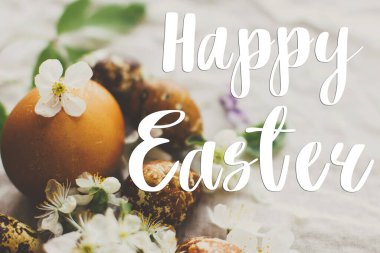 Çağdaş sarı ve kahverengi paskalya yumurtaları üzerine mutlu paskalya metinleri bahar çiçekleri ve kır kumaşında çiçekler, el yazısı. Güzel, şık bir tebrik kartı. Mevsimler selamlar