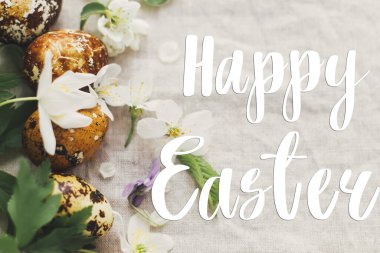 Çağdaş sarı ve kahverengi paskalya yumurtaları üzerine mutlu paskalya metinleri bahar çiçekleri ve kır kumaşında çiçekler, el yazısı. Güzel, şık bir tebrik kartı. Mevsimler selamlar