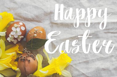 Paskalya yumurtaları üzerine Mutlu Paskalya metinleri. Kırsal peçeteye süslenmiş çiçekler, sarı nergis çiçekleri, düz uzanma, el yazısı. Güzel, şık bir tebrik kartı. Mevsimler selamlar