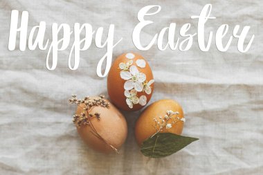 Paskalya yumurtaları üzerine mutlu paskalya metinleri keten peçeteye süslenmiş çiçekler, minimalist düz uzanma, el yazısı. Güzel, şık bir tebrik kartı. Mevsimler selamlar