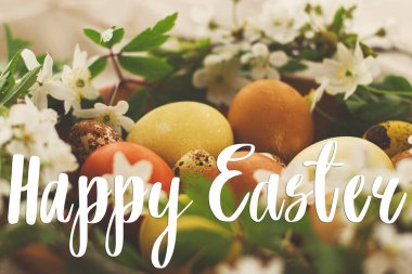 Modern Paskalya yumurtaları üzerine mutlu paskalya metinleri ahşap kasede bahar çiçekleri kırsal çarşaf bezinde el yazısıyla yazılmış. Güzel, şık bir tebrik kartı. Mevsimler selamlar