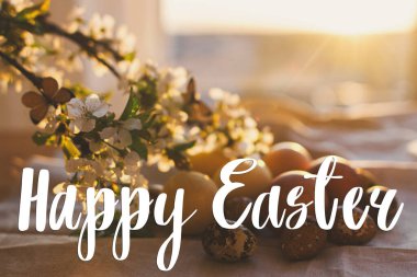 Modern pastel paskalya yumurtaları üzerine Mutlu Paskalya metinleri, kırsal masada kiraz çiçekleri gün batımı ışığında, el yazısıyla. Güzel, şık bir tebrik kartı. Mevsimler selamlar