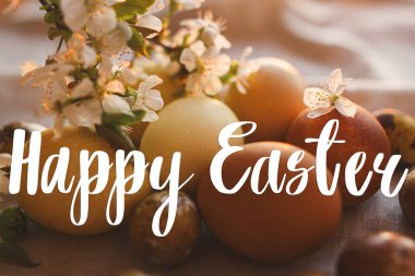 Modern pastel paskalya yumurtaları üzerine Mutlu Paskalya metinleri, kırsal masada kiraz çiçekleri gün batımı ışığında, el yazısıyla. Güzel, şık bir tebrik kartı. Mevsimler selamlar