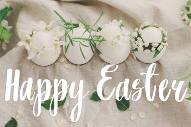 Doğal yumurtalar üzerine mutlu paskalya metinleri keten kumaşında, kiraz çiçekleri ve el yazısıyla yazılmış beyaz taçyaprakları olan hoş çiçekli çelenkler. Güzel, şık bir tebrik kartı. Mevsimler selamlar