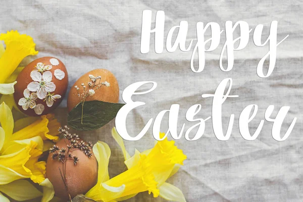 Paskalya yumurtaları üzerine Mutlu Paskalya metinleri. Kırsal peçeteye süslenmiş çiçekler, sarı nergis çiçekleri, düz uzanma, el yazısı. Güzel, şık bir tebrik kartı. Mevsimler selamlar