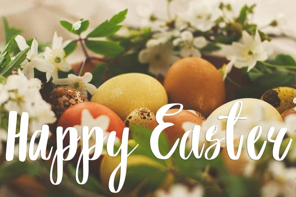 Modern Paskalya yumurtaları üzerine mutlu paskalya metinleri ahşap kasede bahar çiçekleri kırsal çarşaf bezinde el yazısıyla yazılmış. Güzel, şık bir tebrik kartı. Mevsimler selamlar