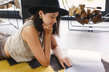 Güzel, şık bir kadın şöminenin arka planında kitap okuyor ve modern dağ evinde büyük bir pencere var. Genç bir bayan, günlük giysiler içinde, dergi ile rahat bir halının üzerinde dinleniyor. Boş zaman ve tatil