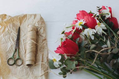 Anneler Günün kutlu olsun. Süslü kırmızı laleler, nergis ve okaliptüs buketi kağıt, makas ve kırsal beyaz ahşap arka planda sicim. Mutlu Kadınlar Günü. Buket yapıyorum.