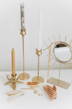 Boho aksesuarları, dahili detaylar. Modern altın mücevherler, beyaz masa üzerinde saç tokaları klasik mumlar ve boho aynası. Şık altın yüzük, zincir kolye, küpeler, saç tokaları ve tokalar..