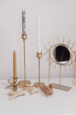 Boho aksesuarları, dahili detaylar. Modern altın mücevherler, beyaz masa üzerinde saç tokaları klasik mumlar ve boho aynası. Şık altın yüzük, zincir kolye, küpeler, saç tokaları ve tokalar..