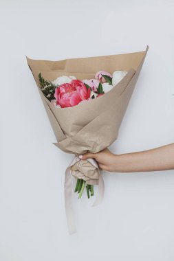 Beyaz duvarın arka planında el ele tutuşmuş güzel, zarif şakayıklar. Kadın elinde pembe ve beyaz şakayık buketi. Anneler Günün kutlu olsun.