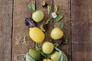 Taze elma, limon, avokado, kırsal ahşap manzaraya serpiştirilmiş eko pamuk torbasından salata yaprakları. Çevre dostu sıfır atık alışveriş konsepti. Organik meyve, sebze ve yeşillik yeniden kullanılabilir poşette.
