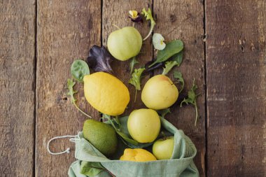 Çevre dostu sıfır atık alışveriş konsepti. Taze elma, limon, avokado, kırsal ahşap üzerine serpiştirilmiş eko pamuk poşetinden salata yaprakları. Salata malzemeleri. Organik meyve, sebze ve yeşillik