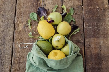 Taze elma, limon, avokado, kırsal ahşap manzaraya serpiştirilmiş eko pamuk torbasından salata yaprakları. Çevre dostu sıfır atık alışveriş konsepti. Organik meyve, sebze ve yeşillik yeniden kullanılabilir poşette.