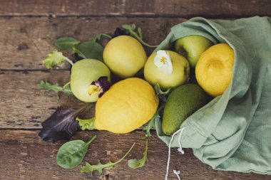Çevre dostu sıfır atık alışveriş konsepti. Taze elma, limon, avokado, kırsal ahşap üzerine serpiştirilmiş eko pamuk poşetinden salata yaprakları. Salata malzemeleri. Organik meyve, sebze ve yeşillik