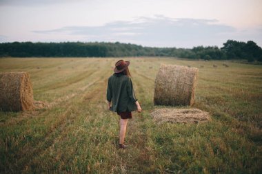 Yaz akşamları saman balyalarında yürüyen şapkalı güzel bir kadın. Mutlu genç bayan samanlıkta dinleniyor, kırsalda tatil yapıyor. Sükunet, kırsal yaşam