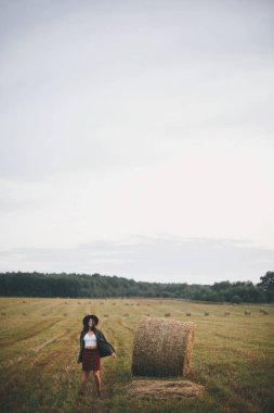 Yaz akşamları saman balyalarında şapkalı güzel bir kadın dans ediyor. Kaygısız mutlu an, kırsalda tatil. Mutlu genç bayan samanlıkta rahatlıyor ve eğleniyor.